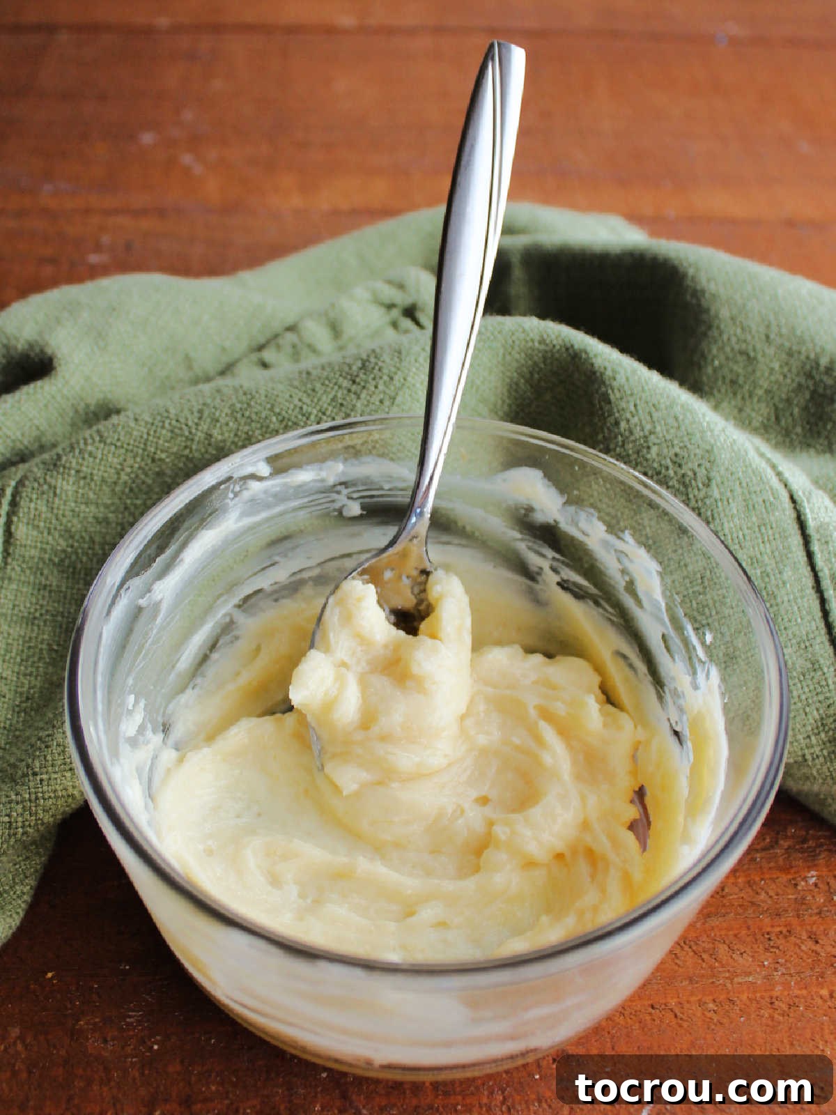 A small, elegant glass bowl filled with the luscious vanilla honey butter, its creamy texture perfectly showcased, with a spoon resting invitingly, ready to spread this delightful concoction on any bread.