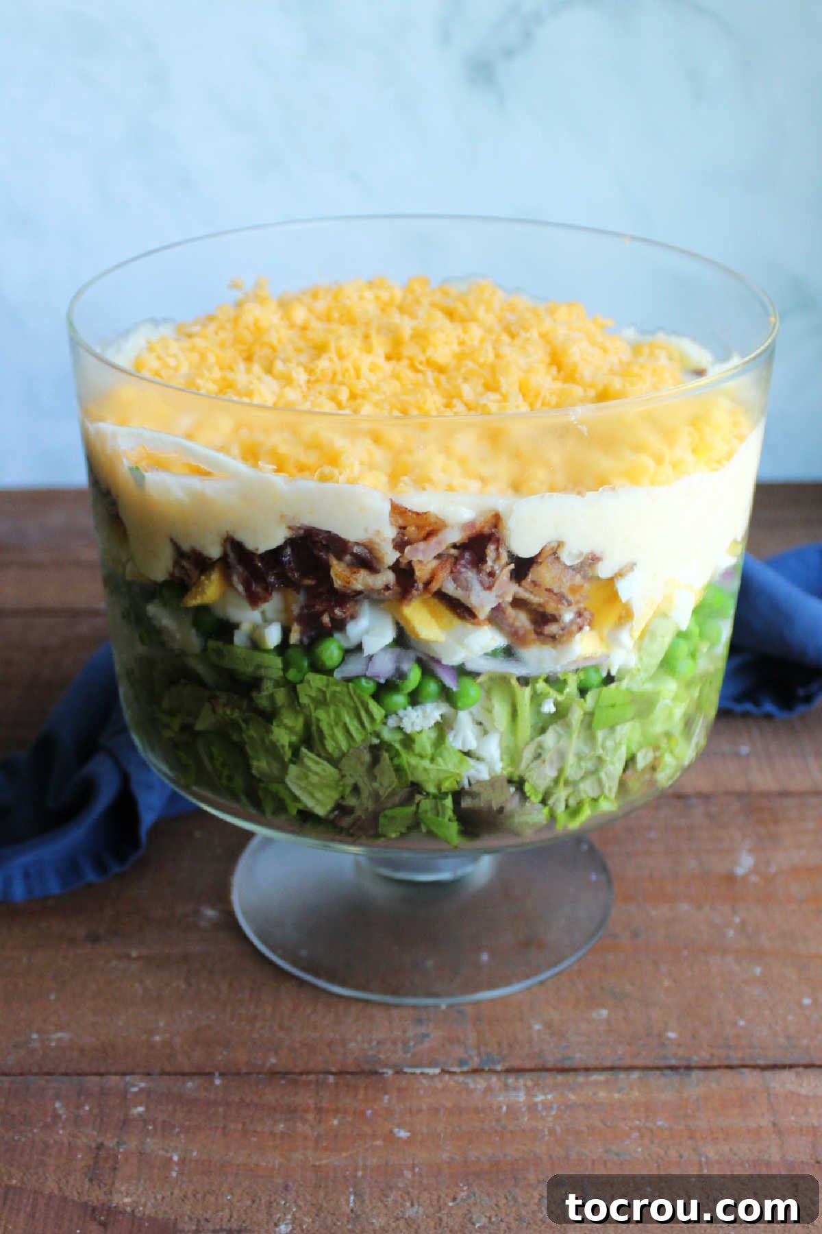 Seven layer salad topped with creamy dressing and freshly shredded cheddar cheese, ready to be served. 