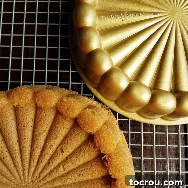 The perfectly golden cinnamon sponge cake, freshly baked and turned out of its elegant Nordic Ware Charlotte-shaped cake pan, showcasing the intricate design.