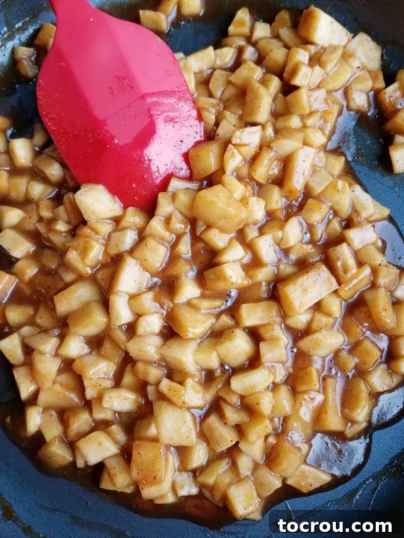 Caramel apple topping, perfectly cooked and glistening in a skillet with a spatula, ready to be gently spread over the cooled cake.