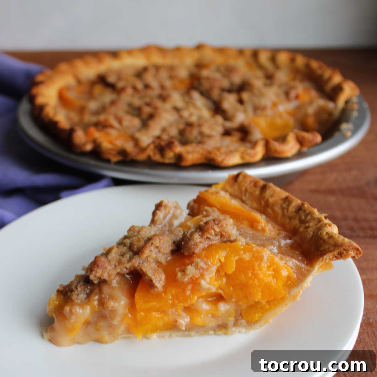 Piece of peach pie with oatmeal crumble topping on plate, ready to eat.