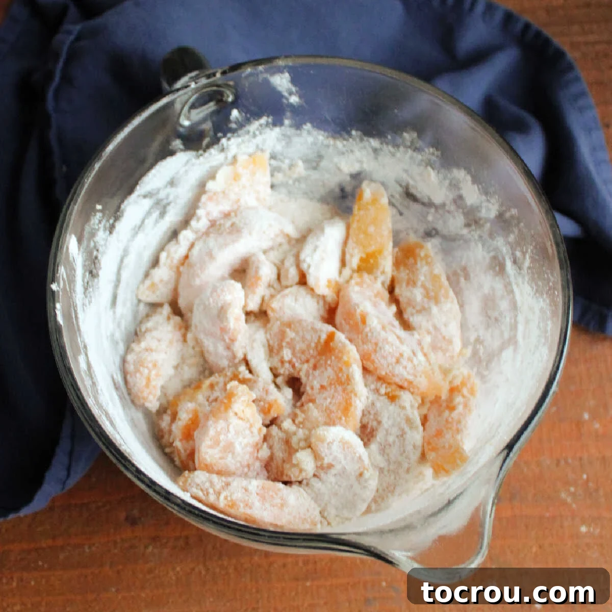 Mixing bowl with peach slices, flour, sugar, and cinnamon ready to go in a pie crust.