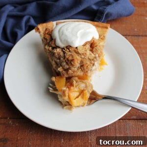 Bite of peach crumble pie with oat topping and on fork next to slice with whipped cream on top.
