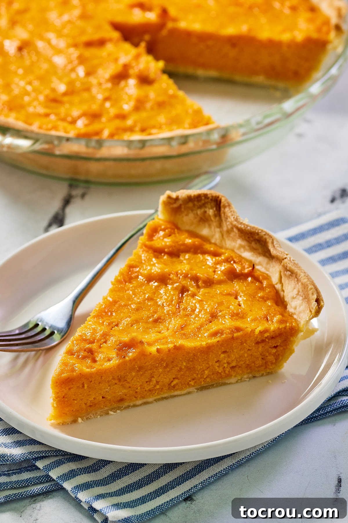 Decadent Sweet Potato Pie with Condensed Milk 3 Slice of sweet potato pie, ready to eat, with remaining pie in pie plate in the background.