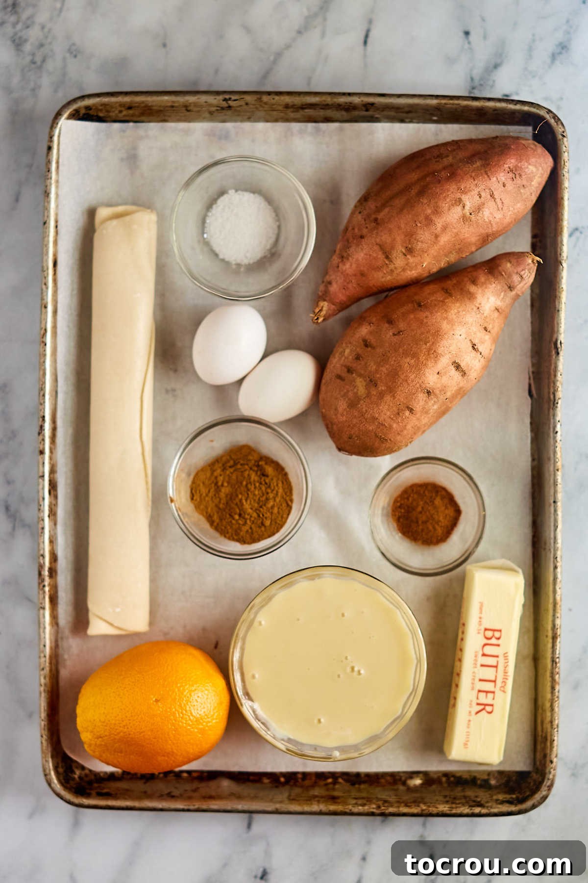 Decadent Sweet Potato Pie with Condensed Milk 5 Tray of ingredients including pie crust, eggs, sweet potatoes, condensed milk, and orange, butter, cinnamon, and nutmeg, ready to be made into a sweet potato pie.