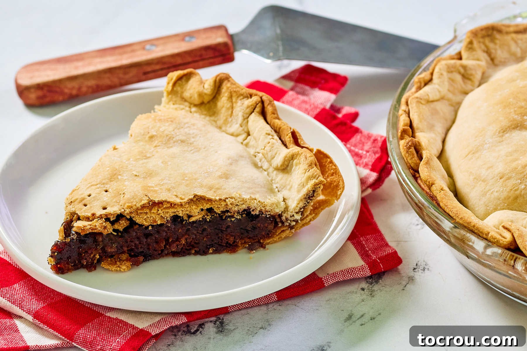 Sweet and Tart Cherry Rhubarb Pie 2 Slice of rhubarb cherry pie on plate with remaining pie and server nearby.