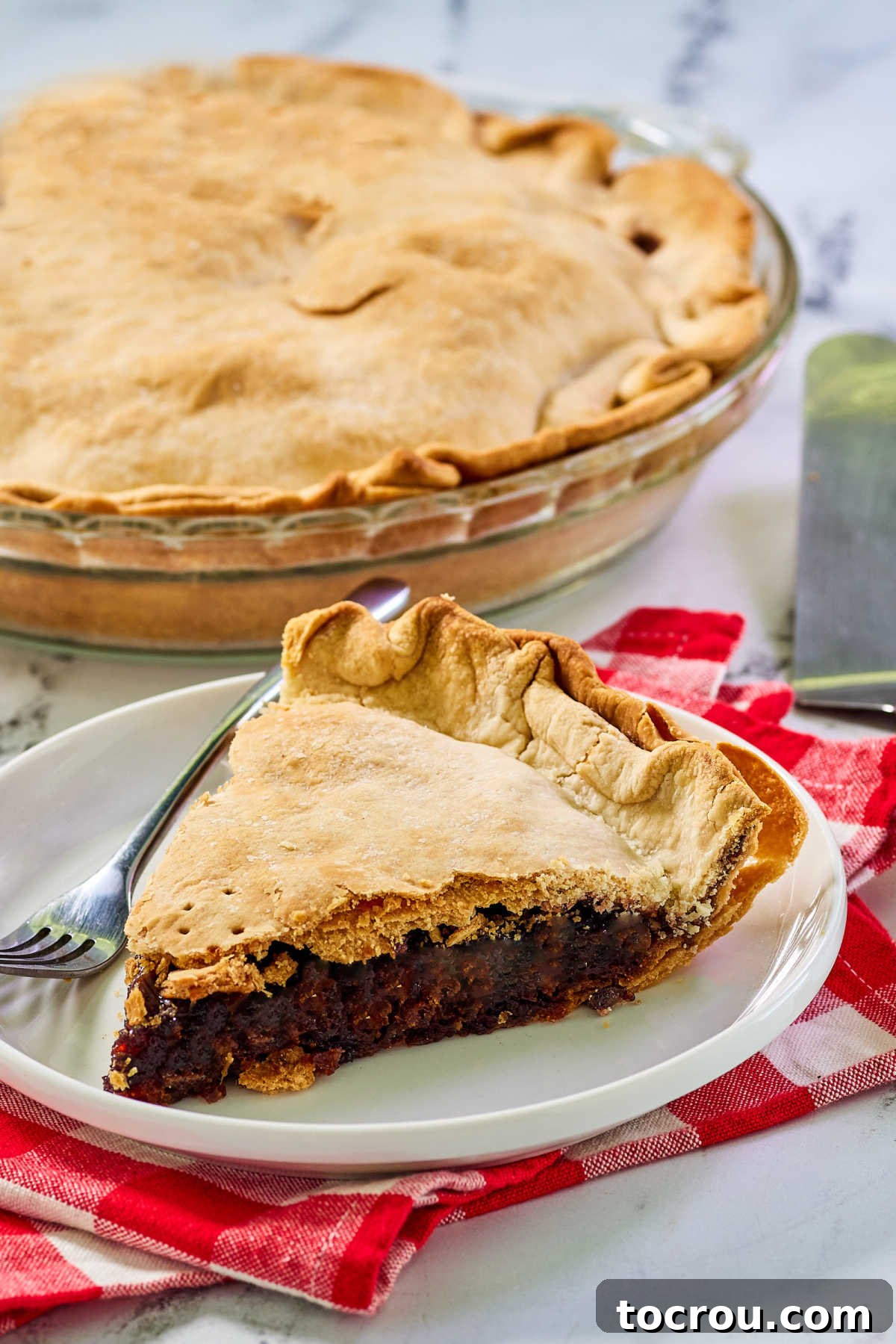 Sweet and Tart Cherry Rhubarb Pie 3 Slice of cherry rhubarb pie on plate with remaining pie in a glass pie plate in the background.