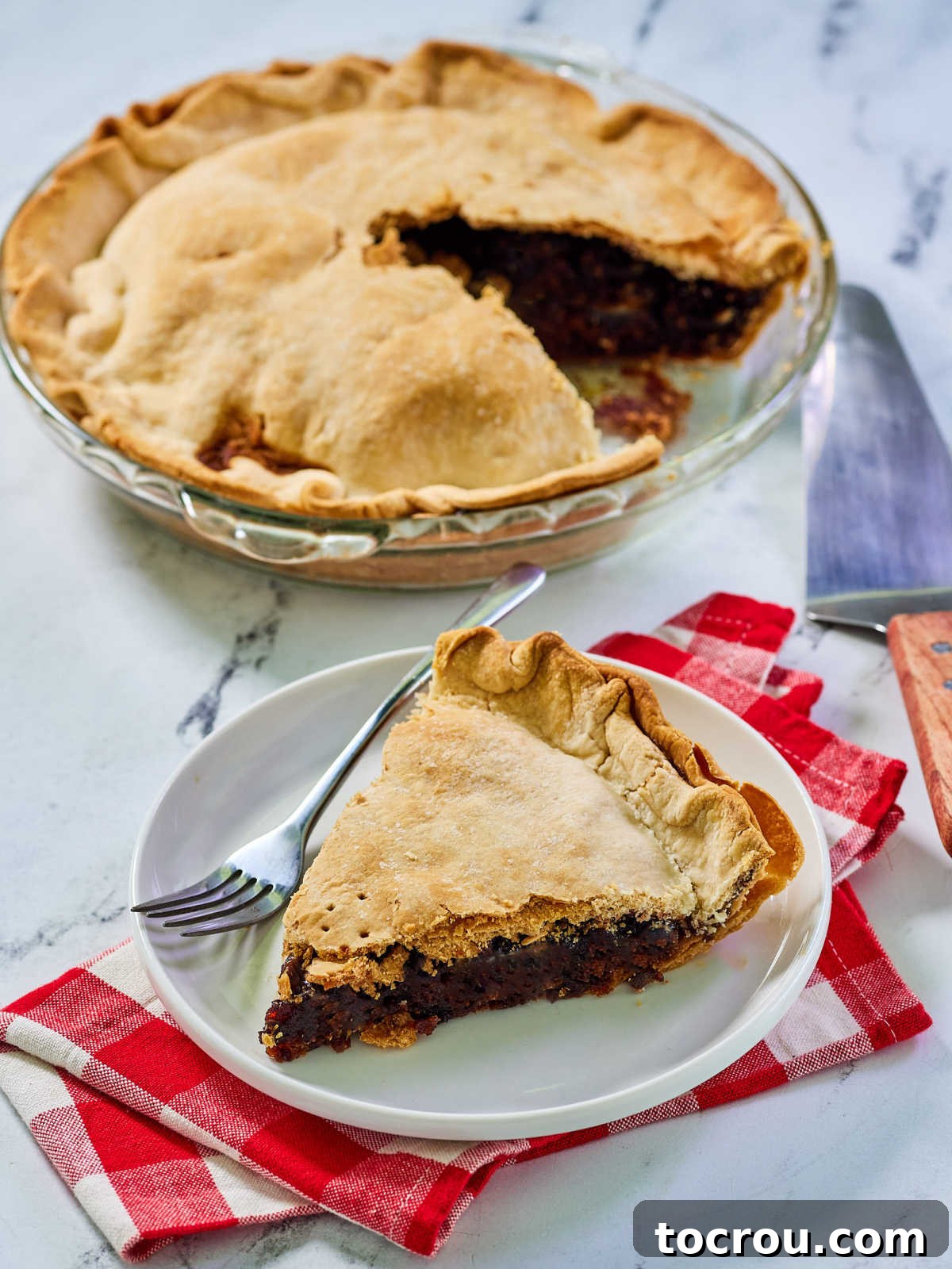 Sweet and Tart Cherry Rhubarb Pie 8 Lookin down on a slice of cherry rhubarb pie with the remaining pie in the background showing the golden brown crust and thickened filling.