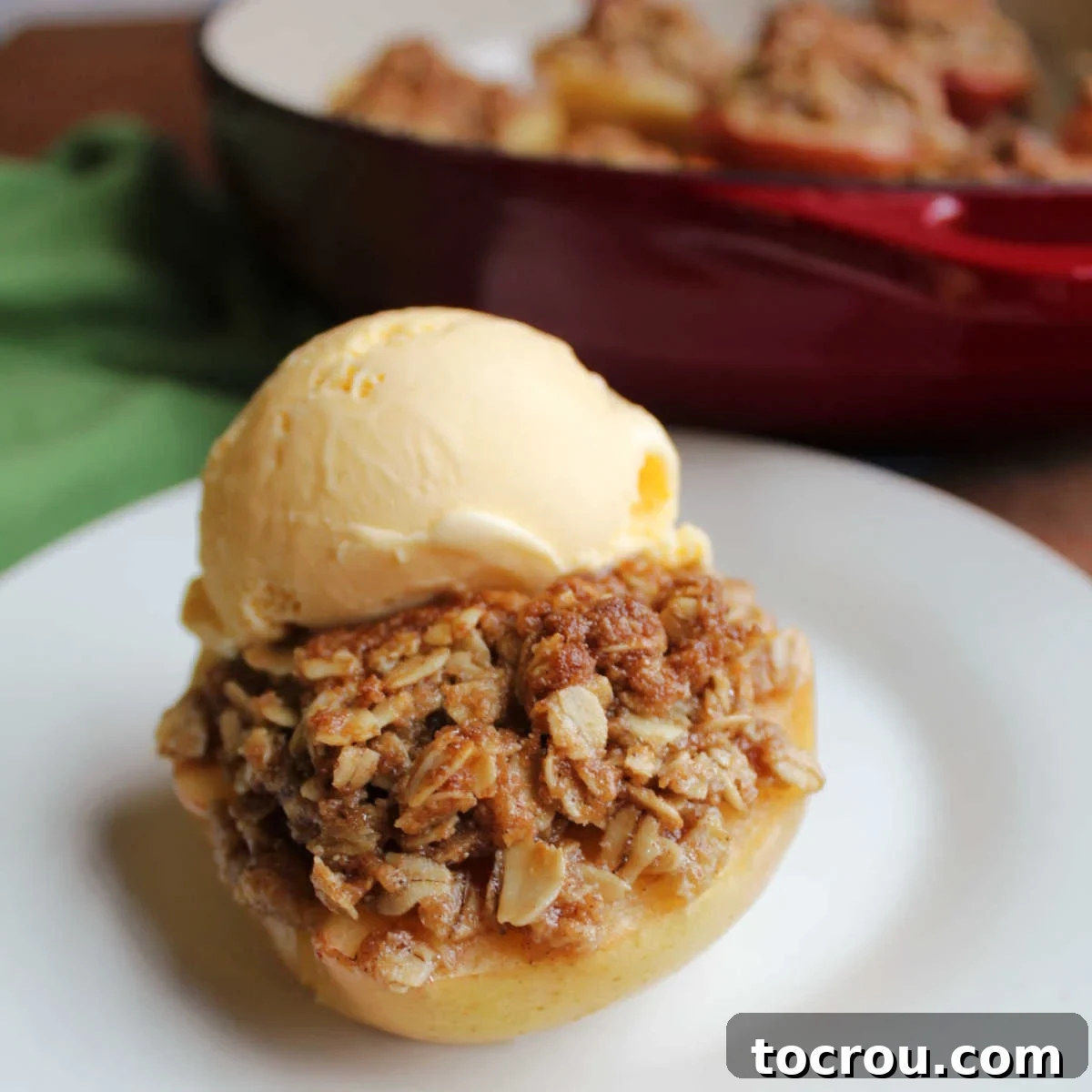 Baked apple half stuffed with brown sugar and oat crisp topping finished with a scoop of vanilla ice cream, ready to eat.