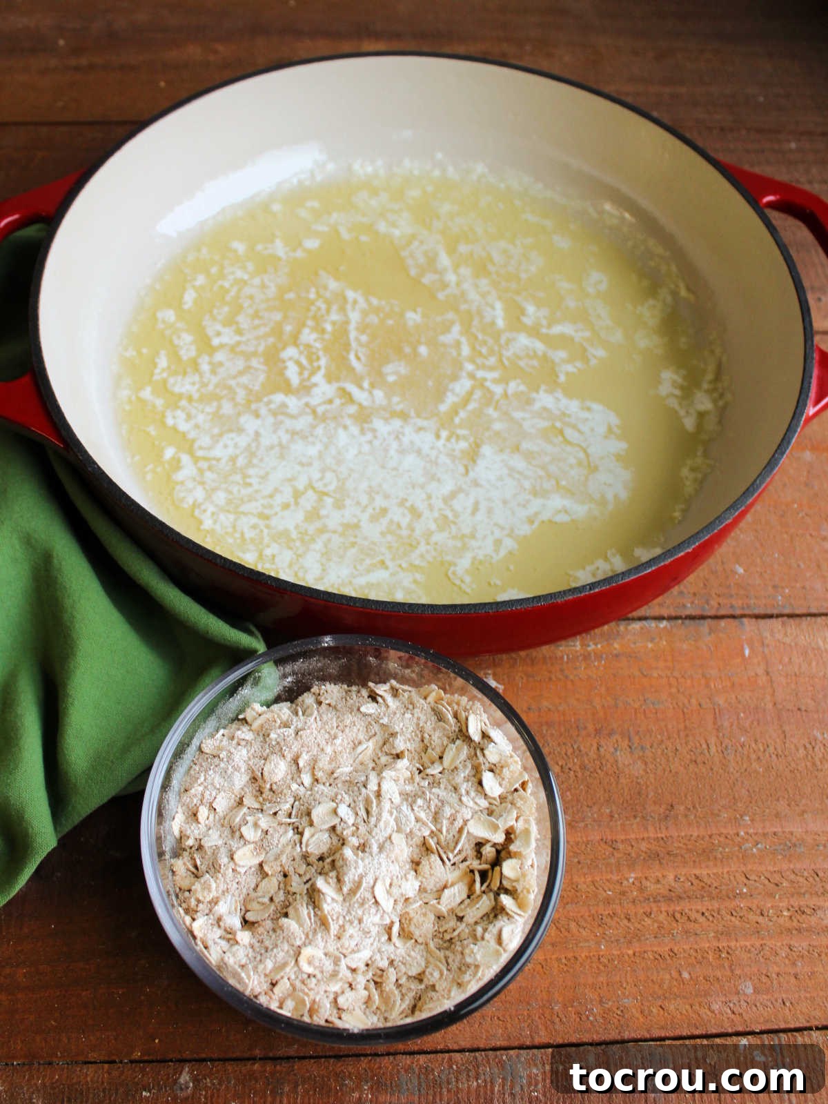Cast iron pan with melted butter by bowl of brown sugar, flour, and oats mixture for crisp filling.