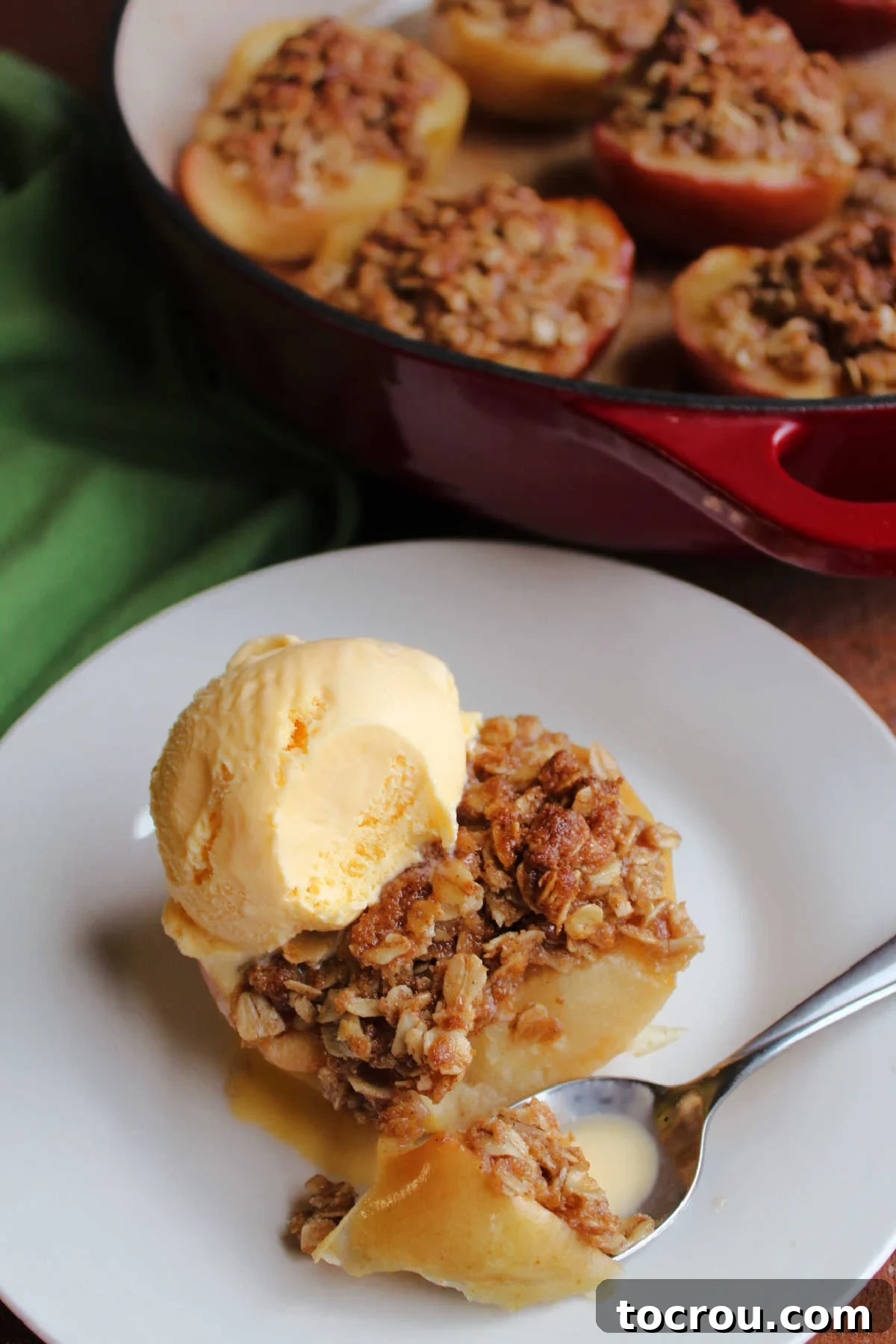 Bite of apple crisp baked apple half on spoon with melted vanilla ice cream showing the softened apple and crisp topping.