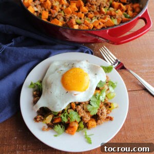 A plate of chorizo hash with peppers, onions, and sweet potatoes topped with fresh cilantro and a fried egg, ready to eat.