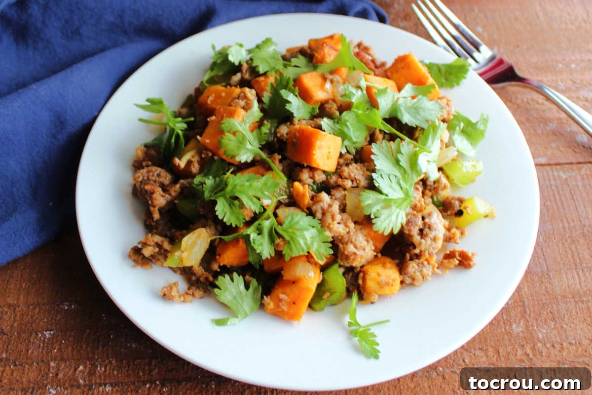 A close-up view of the savory sweet potato hash, showcasing its rich colors and textures. Crumbled chorizo, tender sweet potato cubes, vibrant green bell peppers, and softened onions are visible, all garnished with fresh cilantro.