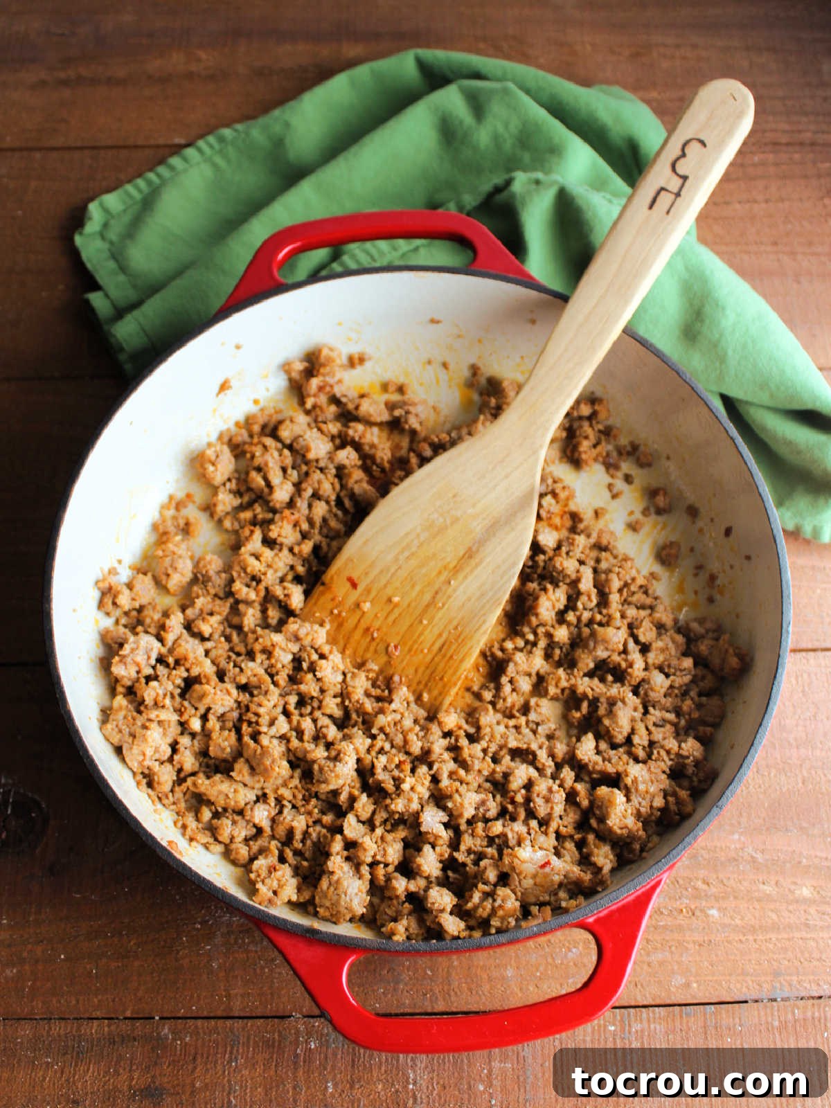 A cast iron skillet contains browned and crumbled Mexican chorizo, with a wooden spatula resting in the pan. The chorizo has released its flavorful oils, creating a rich base for the hash.