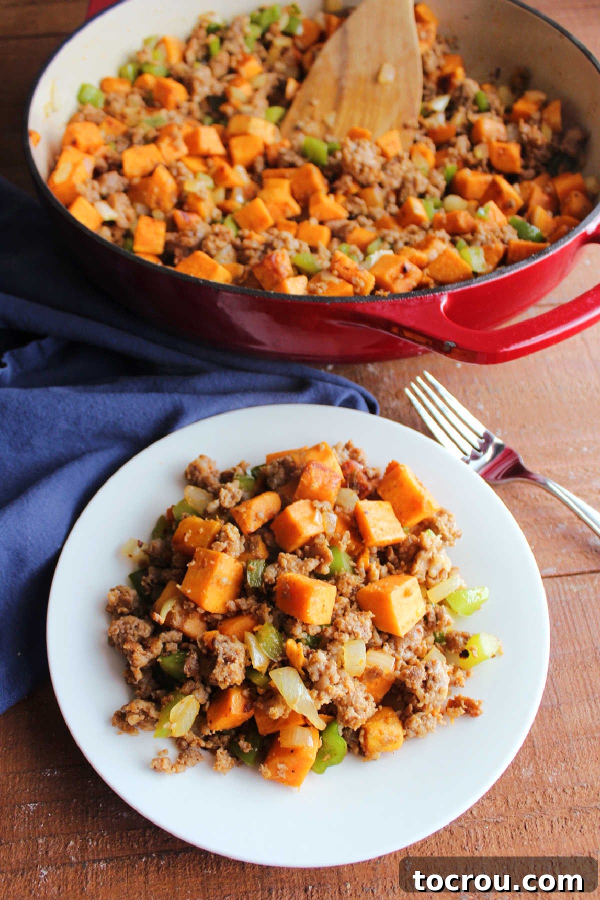 A beautifully plated serving of sweet potato hash with visible cubes of sweet potatoes, green peppers, onions, and crumbled chorizo. In the background, a large skillet holds the remaining hash, suggesting a generous portion for a meal.