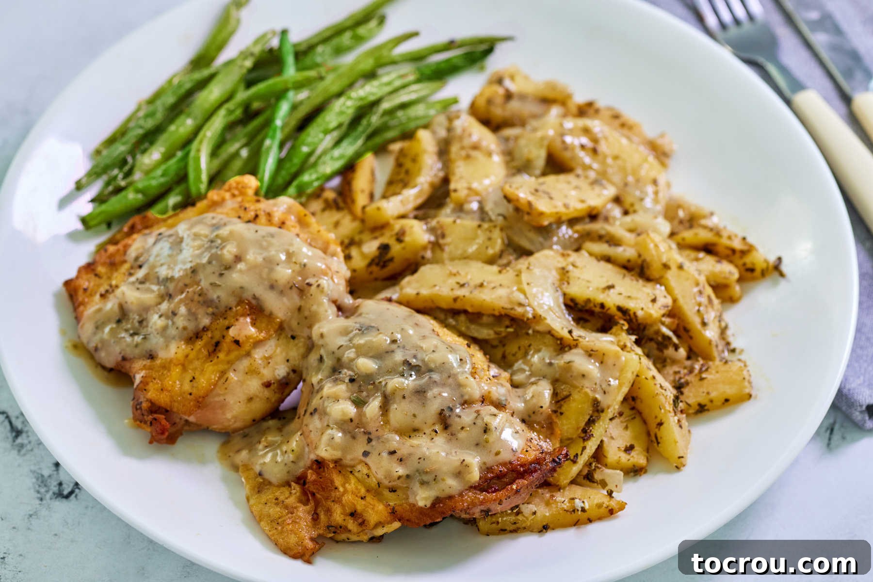 Plate of chicken and apples with an apple cider and mustard pan sauce served with green beans, ready to eat.