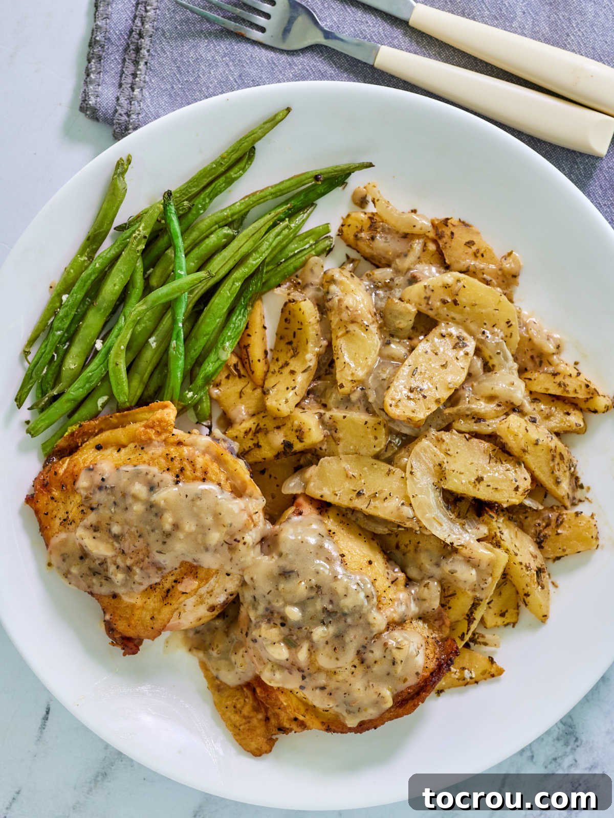 Plate of chicken thighs topped with apple cider and mustard pan sauce served with cooked apples and onions and a side of green beans.