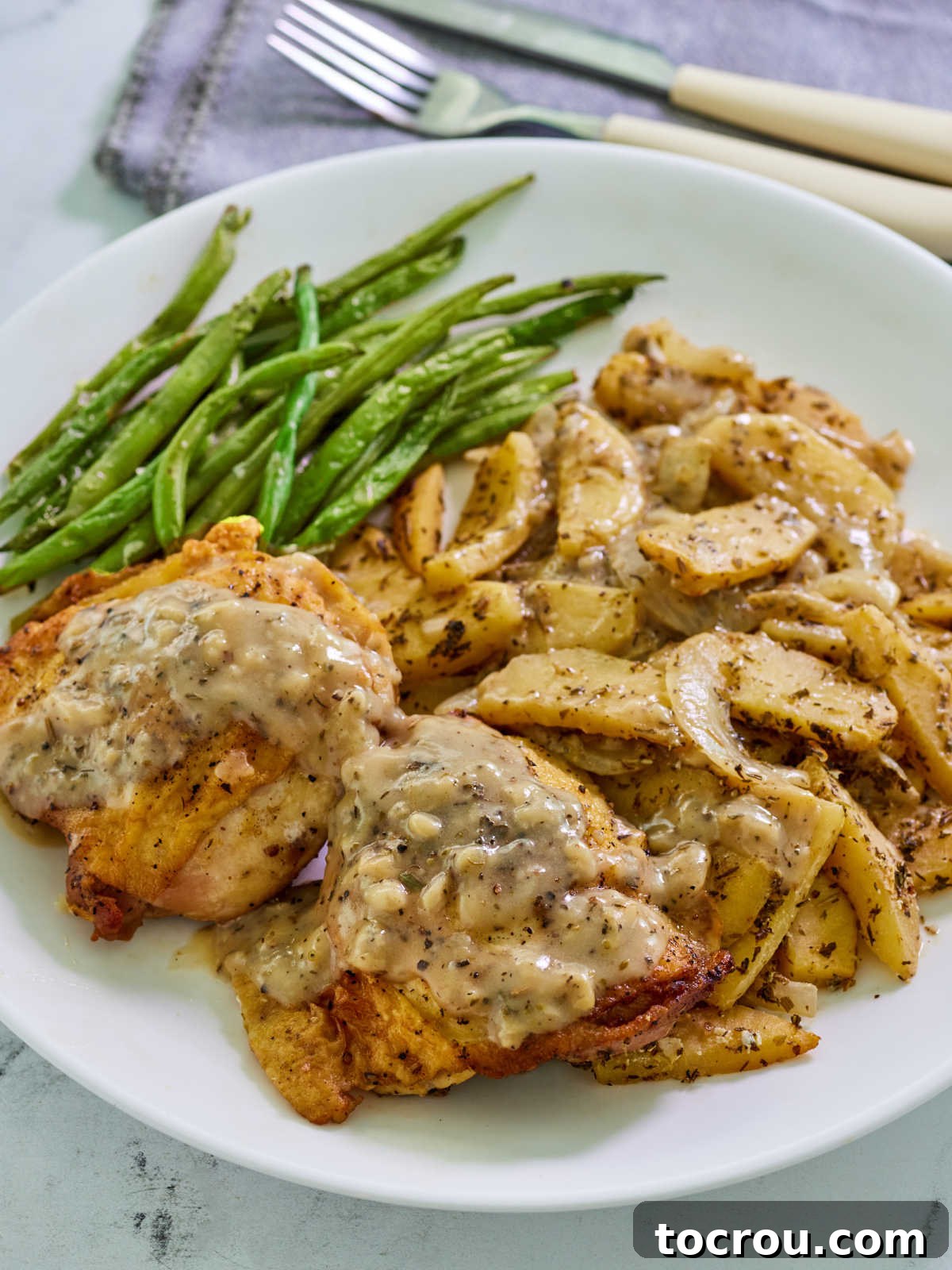 Dinner plate of apple cider chicken with sliced apples and onions, served with green beans, ready to eat.