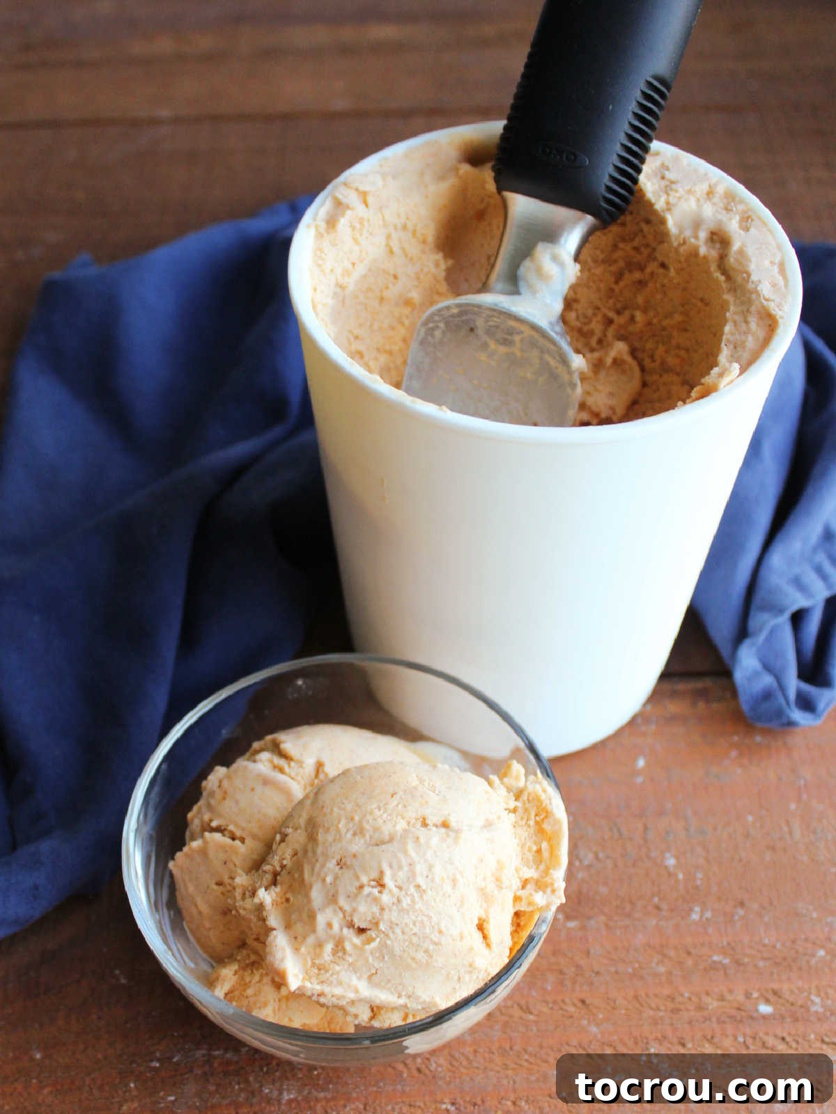 Velvet Pumpkin Ice Cream 6 Scoops of pumpkin ice cream in a small glass bowl with more ice cream and scoop in storage container nearby.