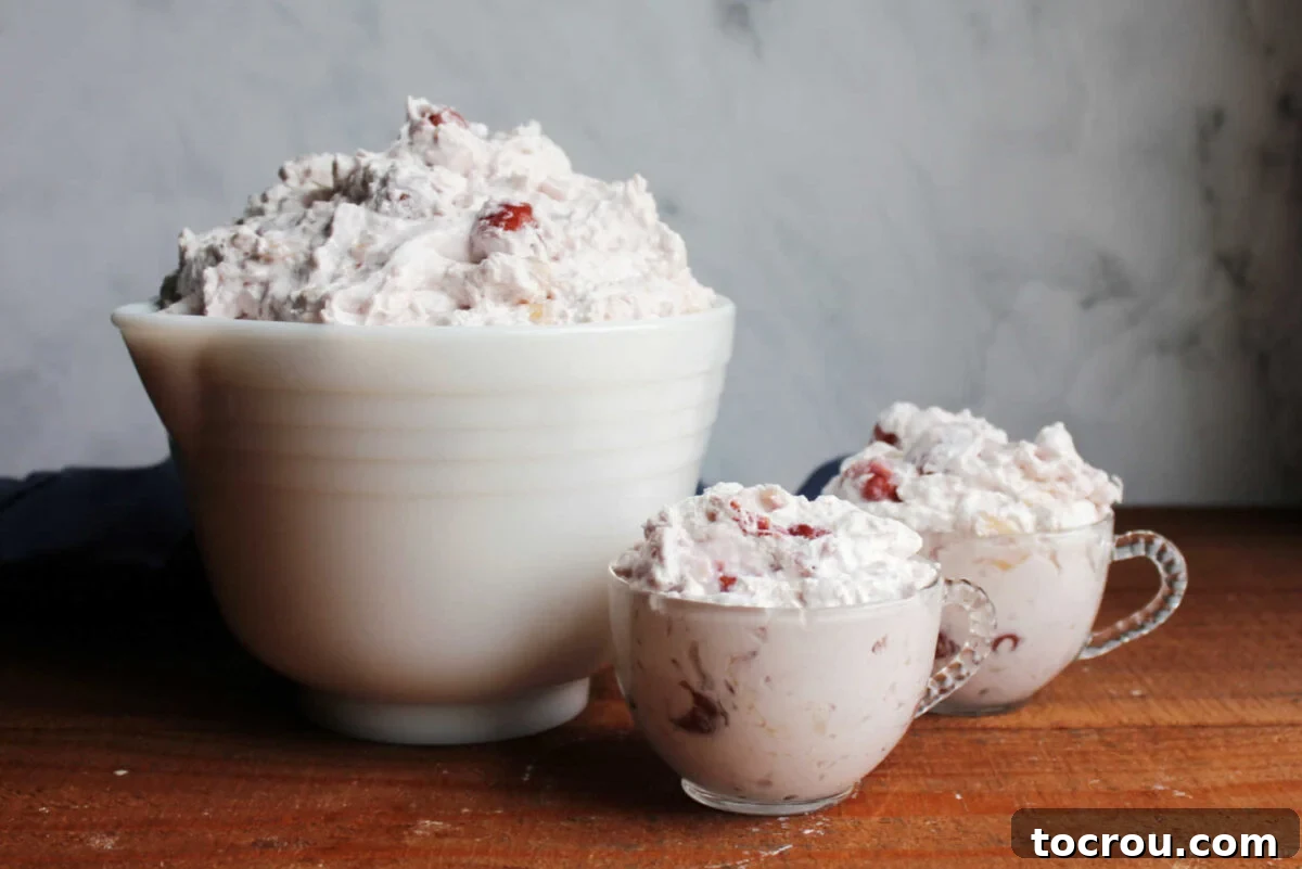 Vintage white serving bowl filled with cherry cheesecake fluff next to two glass punch cups filled with more fluffy cherry cheesecake salad. 
