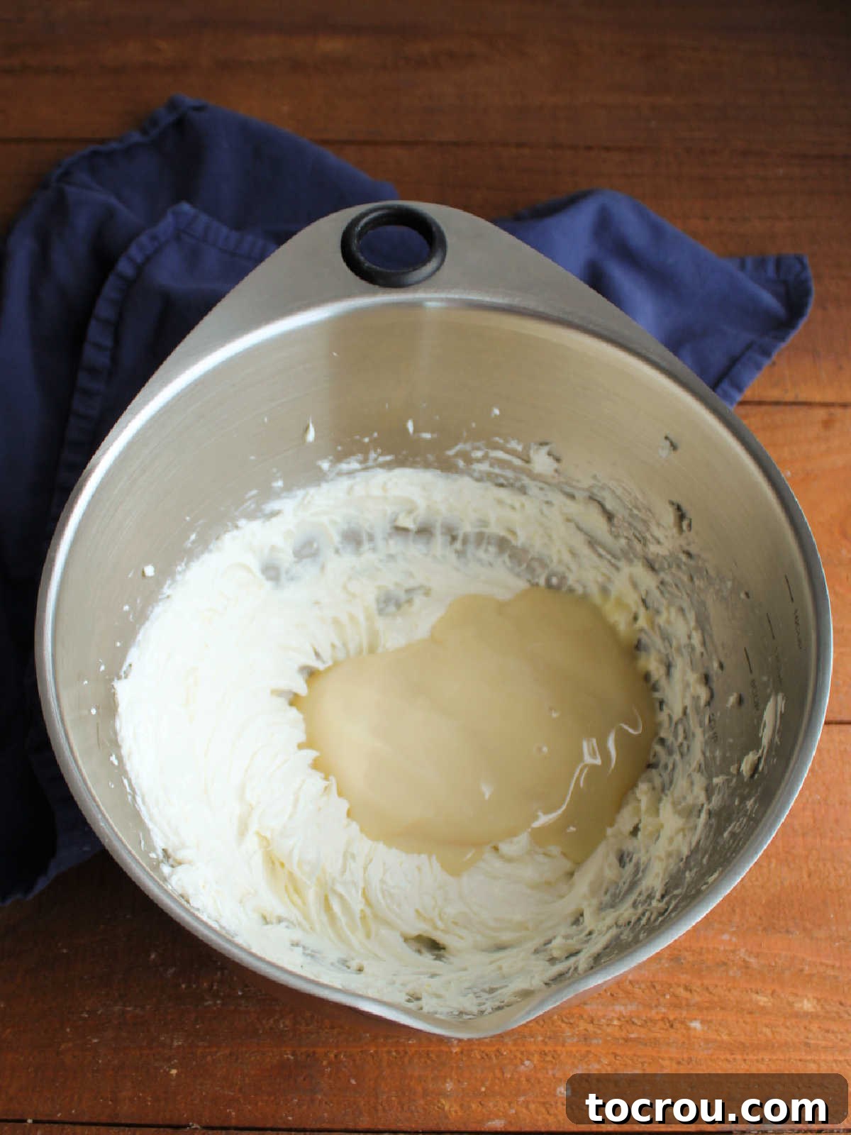 Large mixing bowl with condensed milk and beaten cream cheese, ready to be stirred together. 