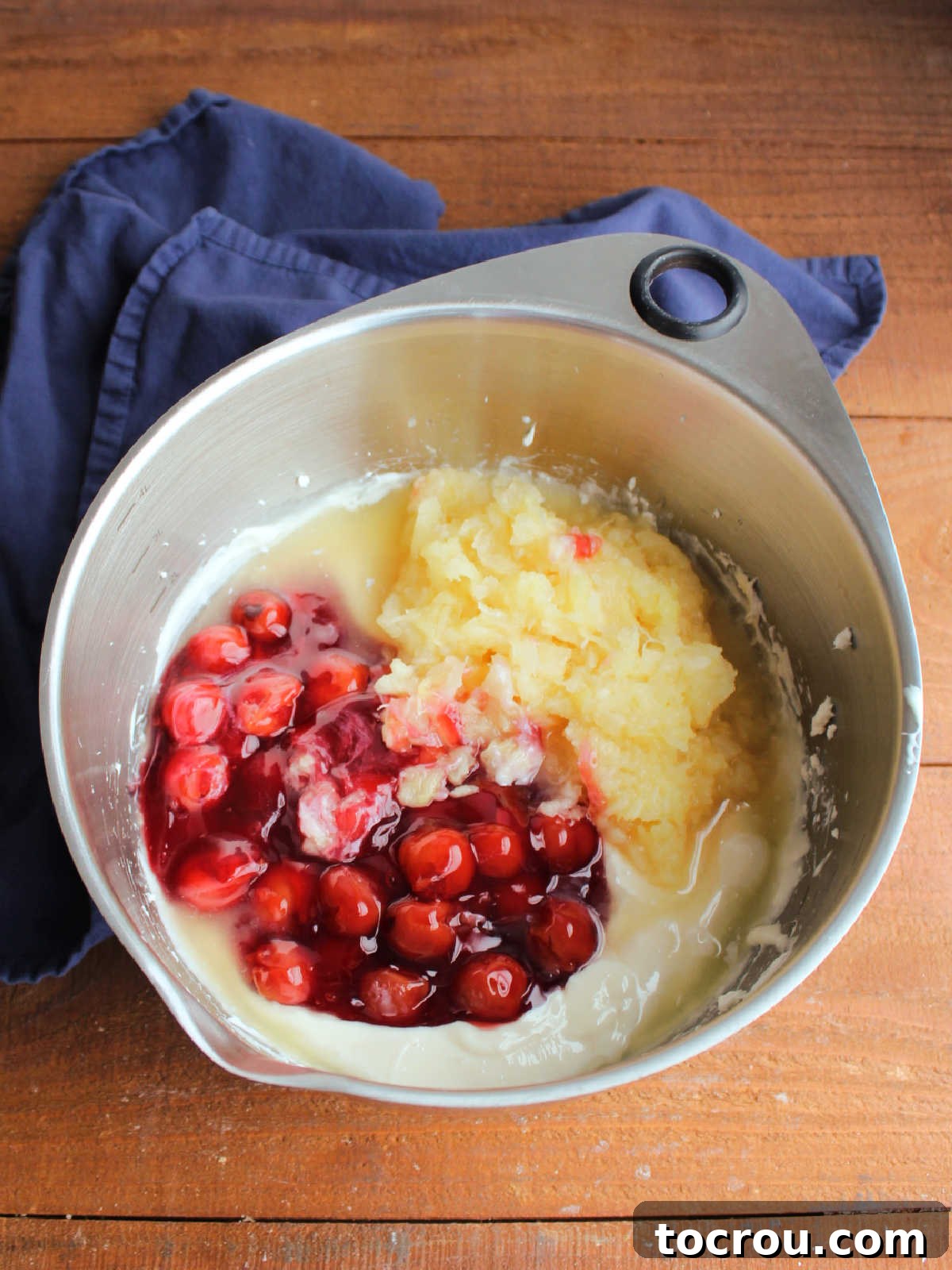 Adding crushed pineapple and cherry pie filling to cream cheese and condensed mixture. 