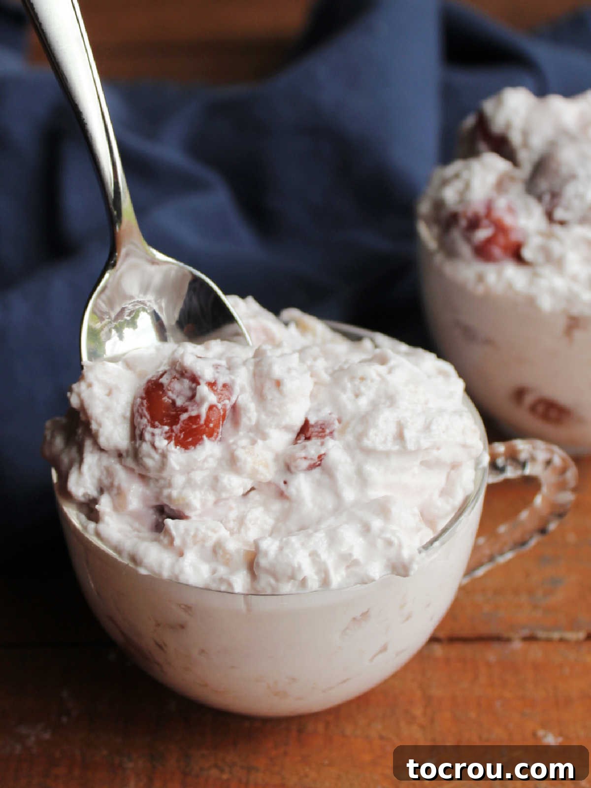 Spoon getting a bite of fluffy cherry cheesecake salad from a cup filled with the creamy fluff salad.