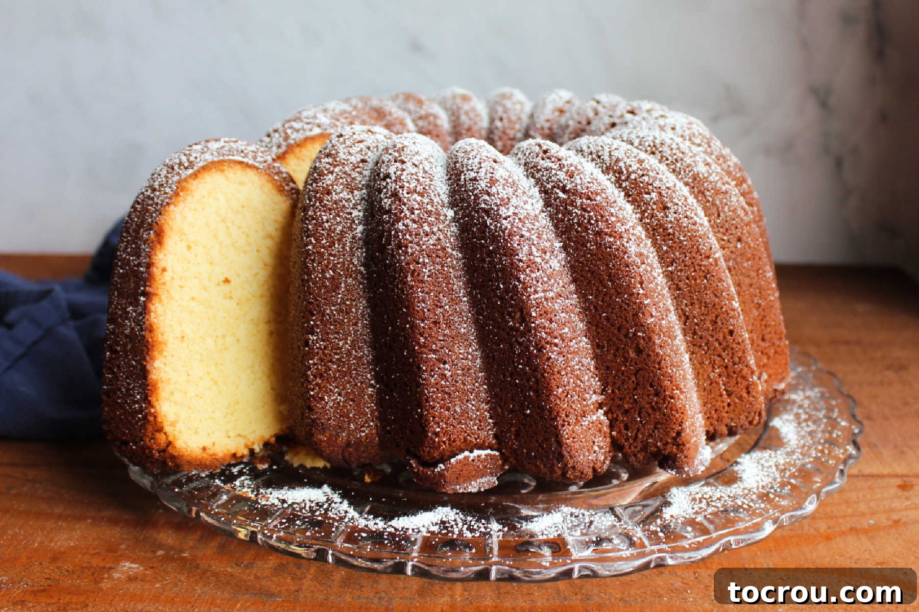 Condensed milk bundt cake dusted with powdered sugar on glass cake plate with one slice pulled out slightly showing brown exterior and light golden colored vanilla cake interior.