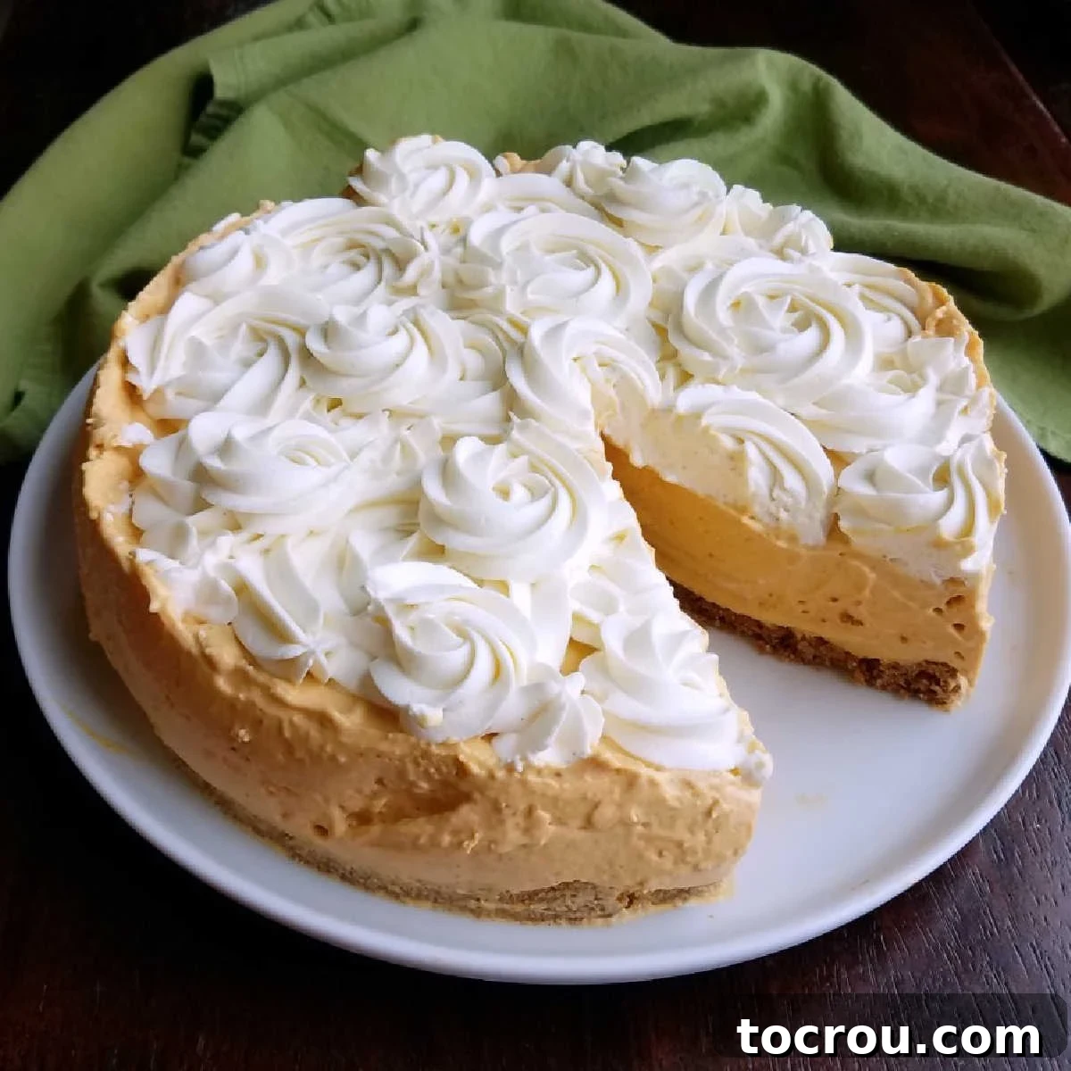 Dreamy No-Bake Pumpkin Cheesecake 2 A whole no-bake pumpkin cheesecake with decorative rosettes of cream cheese whipped cream on top, with one slice carefully removed, revealing the creamy pumpkin filling and crumbly crust.
