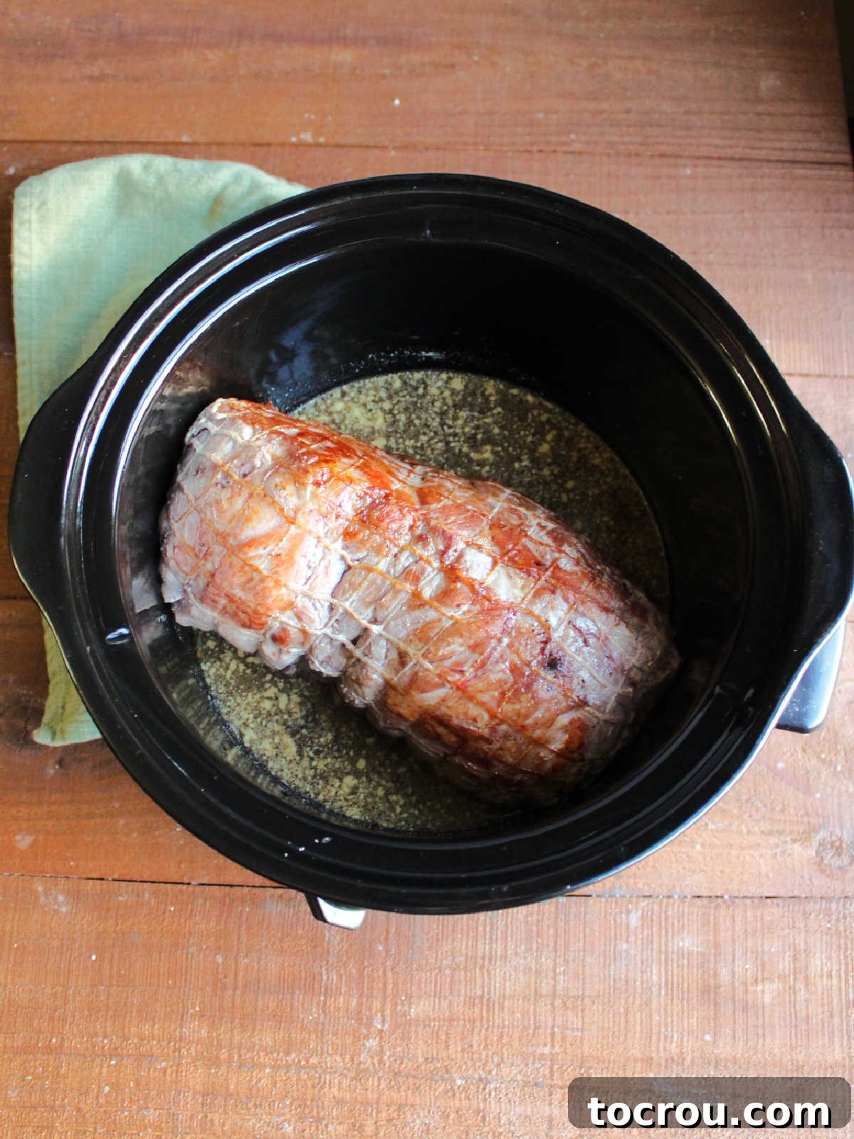 A large crockpot containing a perfectly browned pork roast, surrounded by the aromatic sauce ingredients, poised for slow cooking.