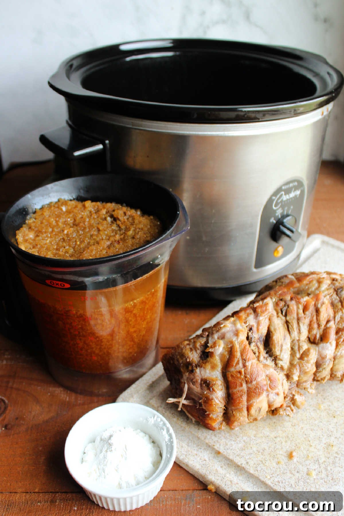 A bowl of cornstarch sits beside a fat separator, efficiently removing grease from the savory cooking liquids, while the tender cooked pork waits to be returned to the crockpot for the final steps of cooking.