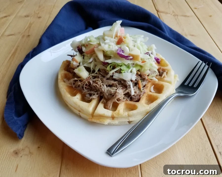 A delicious waffle piled high with apple cider pulled pork and a vibrant apple coleslaw, creating a unique and hearty meal.