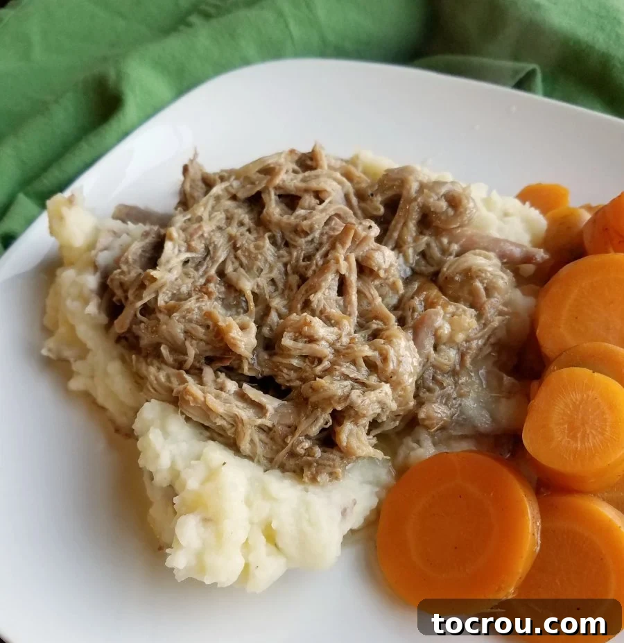 A close-up view of apple cider pulled pork served over creamy mashed potatoes, with tender carrots on the side, highlighting the rich texture and vibrant colors of the dish.