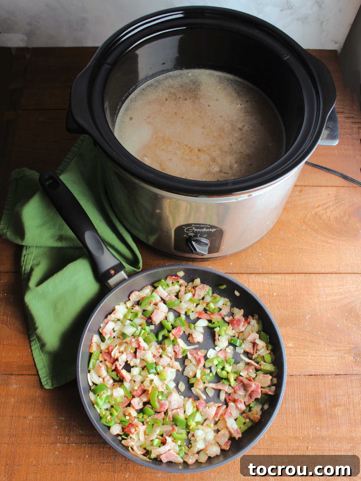Skillet with bits of cooked bacon, diced onion, and jalapenos in it next to crock pot with dried pinto beans, water, beer and seasonings inside ready to combine and cook.
