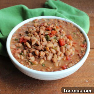 Serving bowl filled with cooked pinto beans in broth made with beer, onions, and jalapenos with bits of diced tomatoes and cilantro mixed in ready to be served as frijoles borrachos.