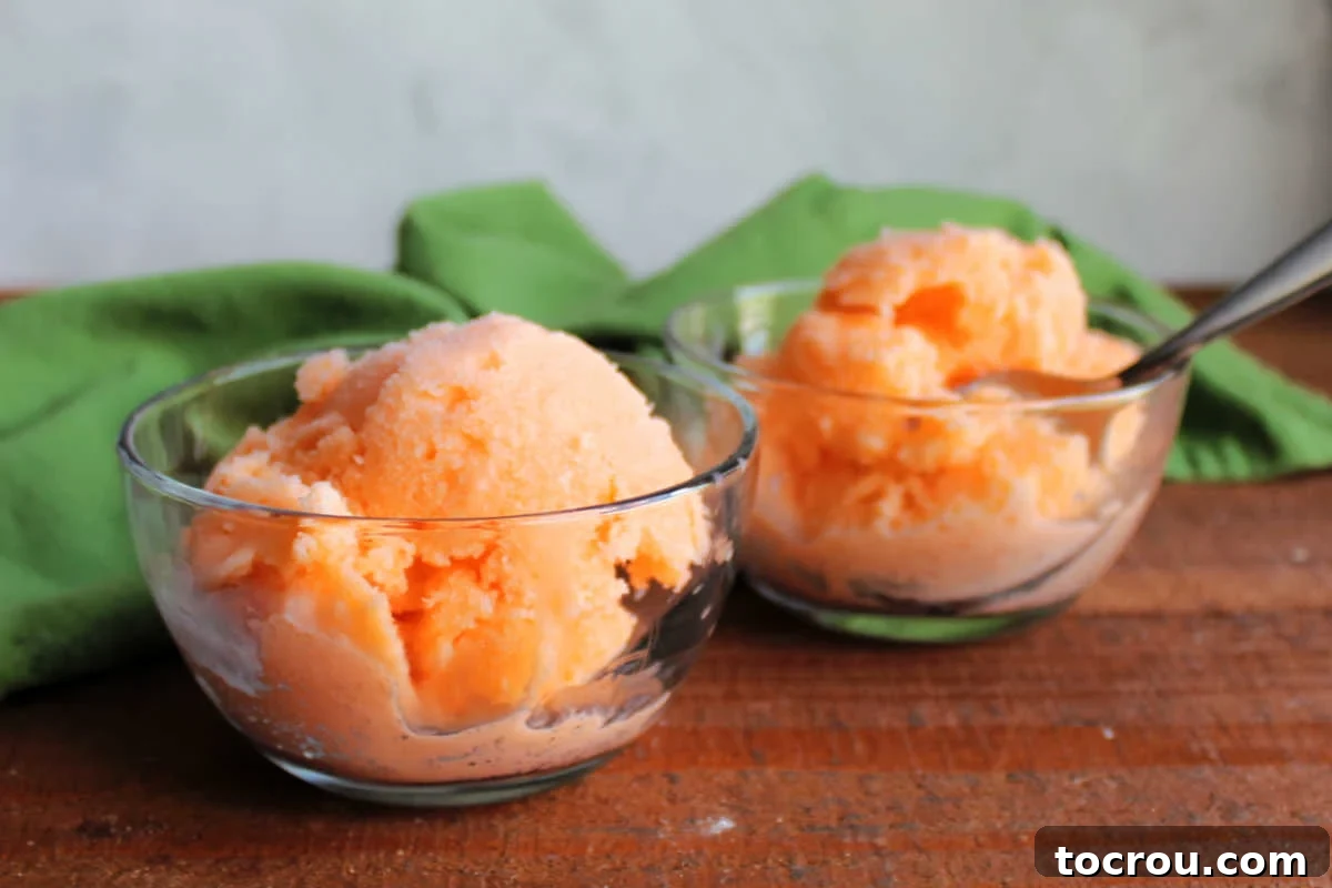 Two glass bowls with scoops of bright orange homemade sherbet inside, ready to eat. 