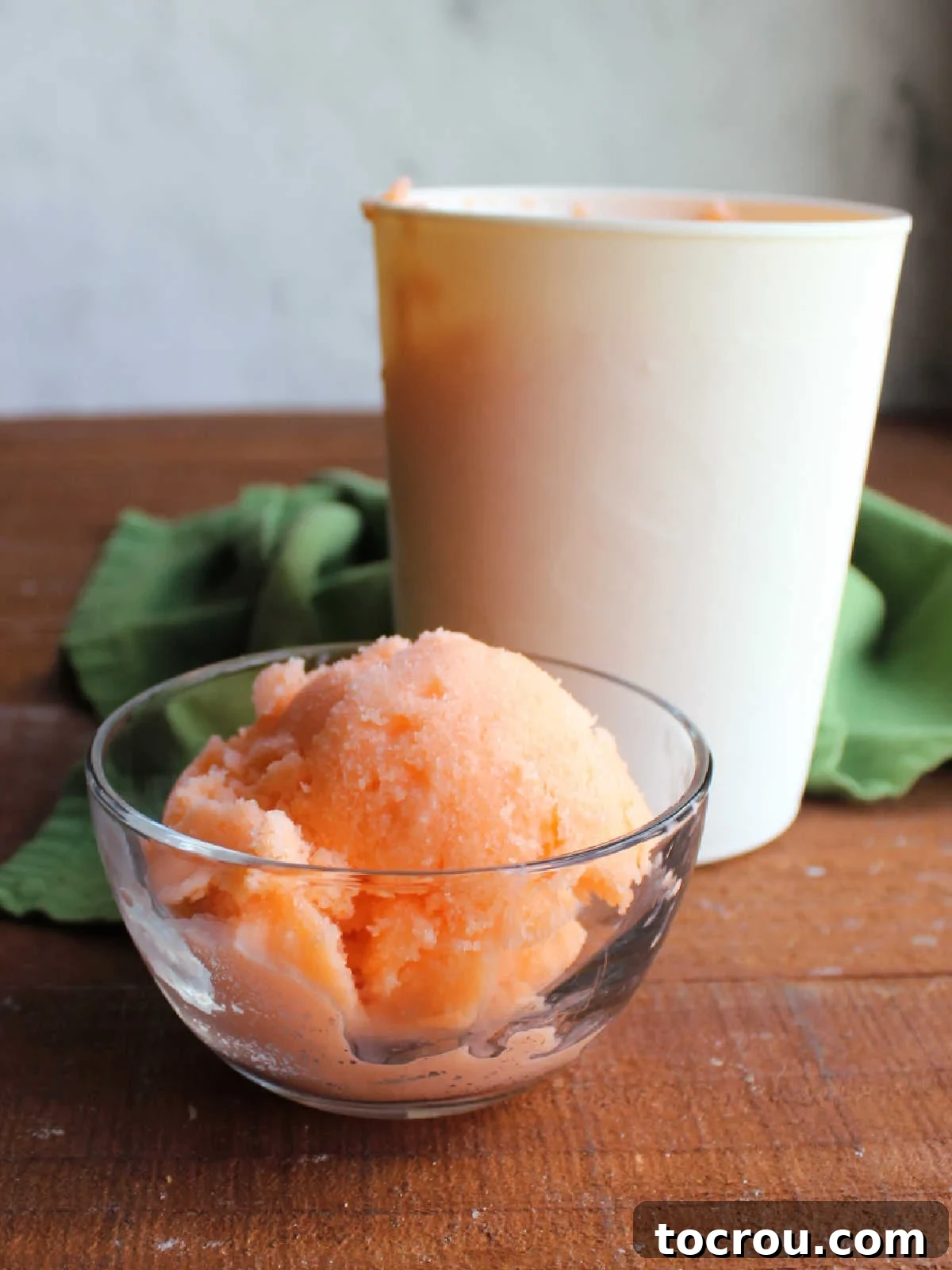 Bowl of 2 ingredient orange sherbet in front of storage container with more sherbet inside. 