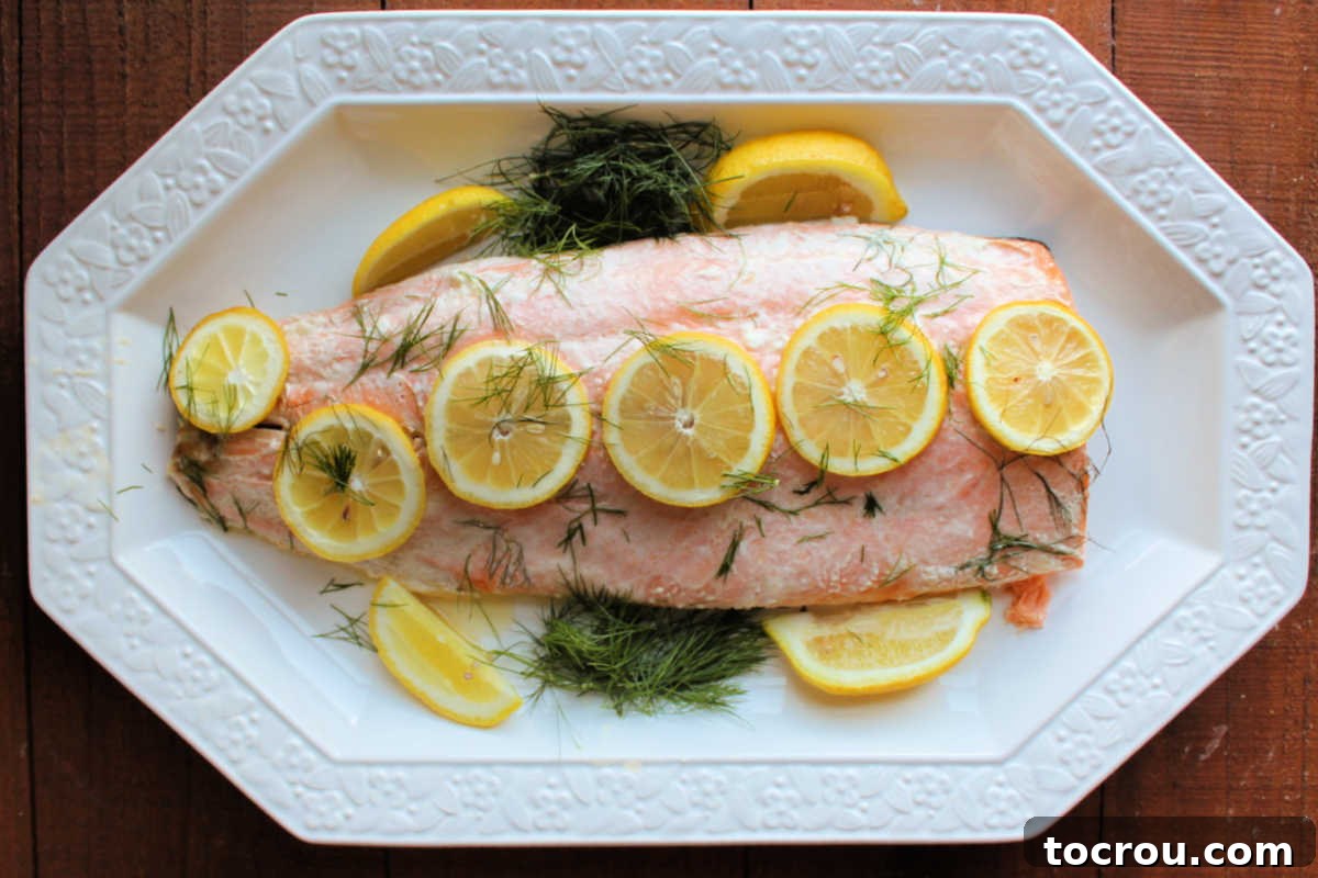 Delicious Baked Salmon with Lemon and Dill A large platter displaying a beautifully baked salmon fillet, garnished with bright lemon slices and fresh green dill sprigs, ready to be served.