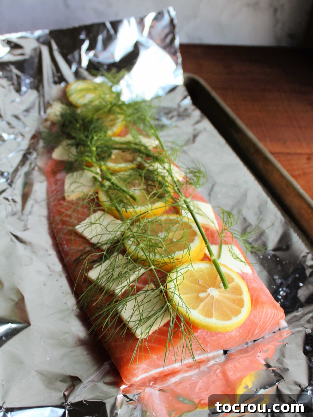 Salmon Prepped for Baking A baking tray lined with aluminum foil, featuring a fresh slab of salmon topped with pats of butter, vibrant lemon slices, and fragrant fresh dill, perfectly prepped for baking.