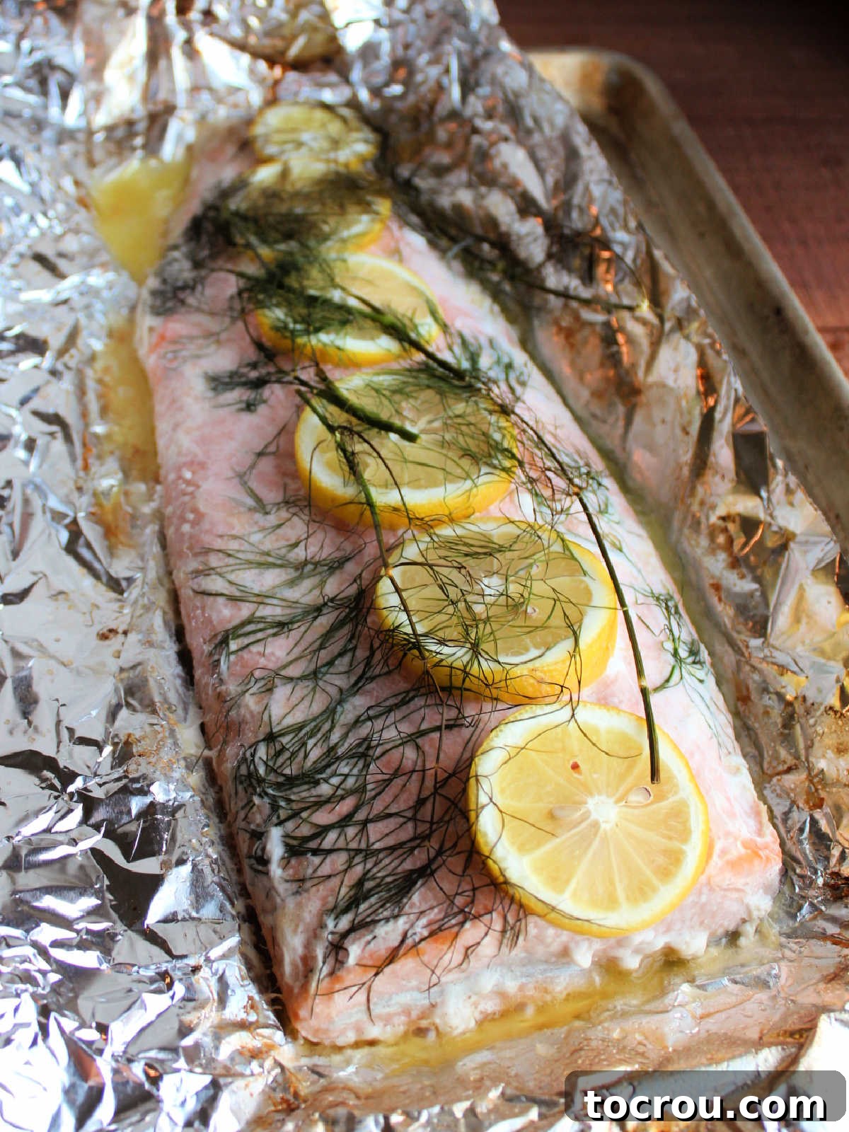 Flaky Cooked Salmon with Lemon and Dill A cooked salmon fillet, now unwrapped from foil, reveals its flaky texture and is beautifully adorned with fresh lemon slices and dill fronds, glistening with butter.