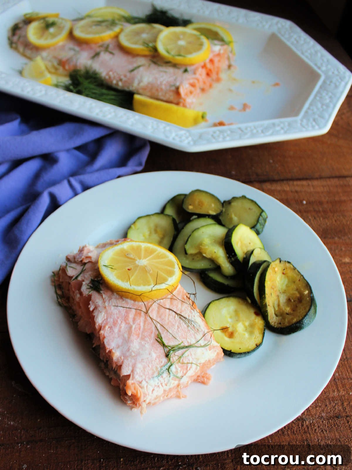 Served Baked Salmon with Zucchini A dinner plate featuring a generous piece of baked salmon, elegantly topped with fresh lemon slices and dill, served alongside perfectly roasted zucchini slices, ready for a delicious and healthy meal.