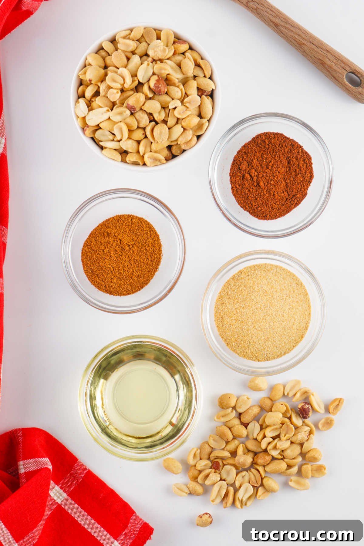 Zesty Peanuts 3 Ingredients including raw peanuts, cooking oil, chili powder, garlic powder, and cayenne pepper laid out on a wooden surface, ready to be prepared into spicy peanuts.