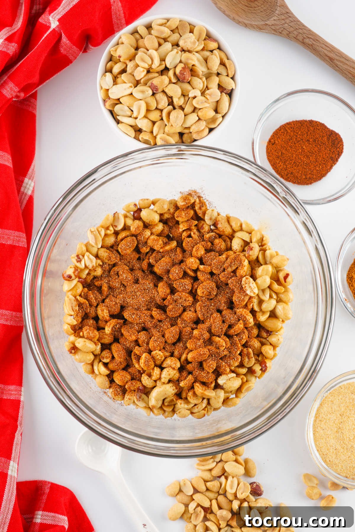 Zesty Peanuts 4 Mixing bowl of oil-coated peanuts with a vibrant pile of chili, garlic, and cayenne spices on top, awaiting a thorough mix before baking.