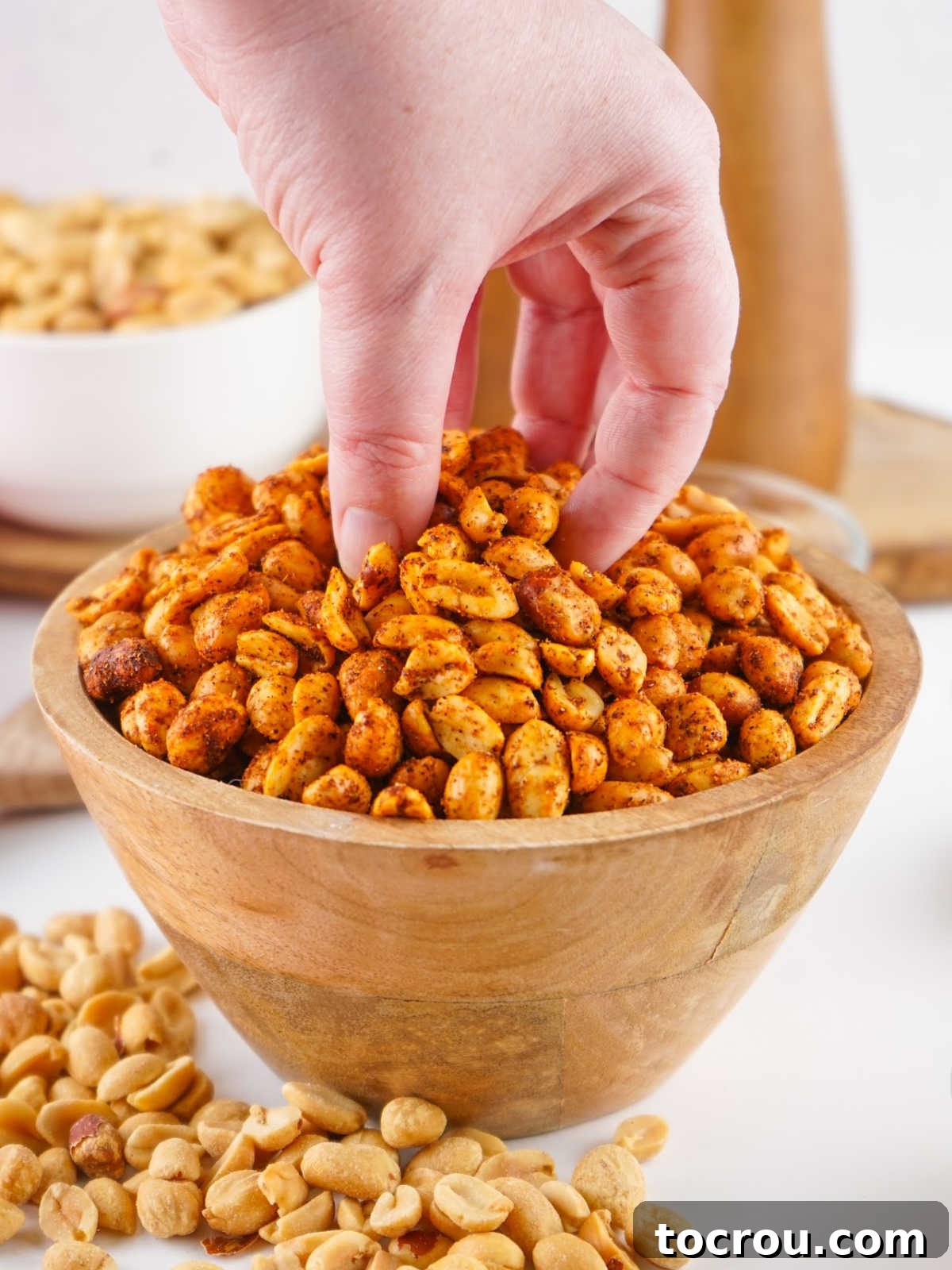 Zesty Peanuts 8 A hand reaching into a rustic bowl filled with golden-brown spiced peanuts, tempting the viewer to grab a handful of the savory snack.