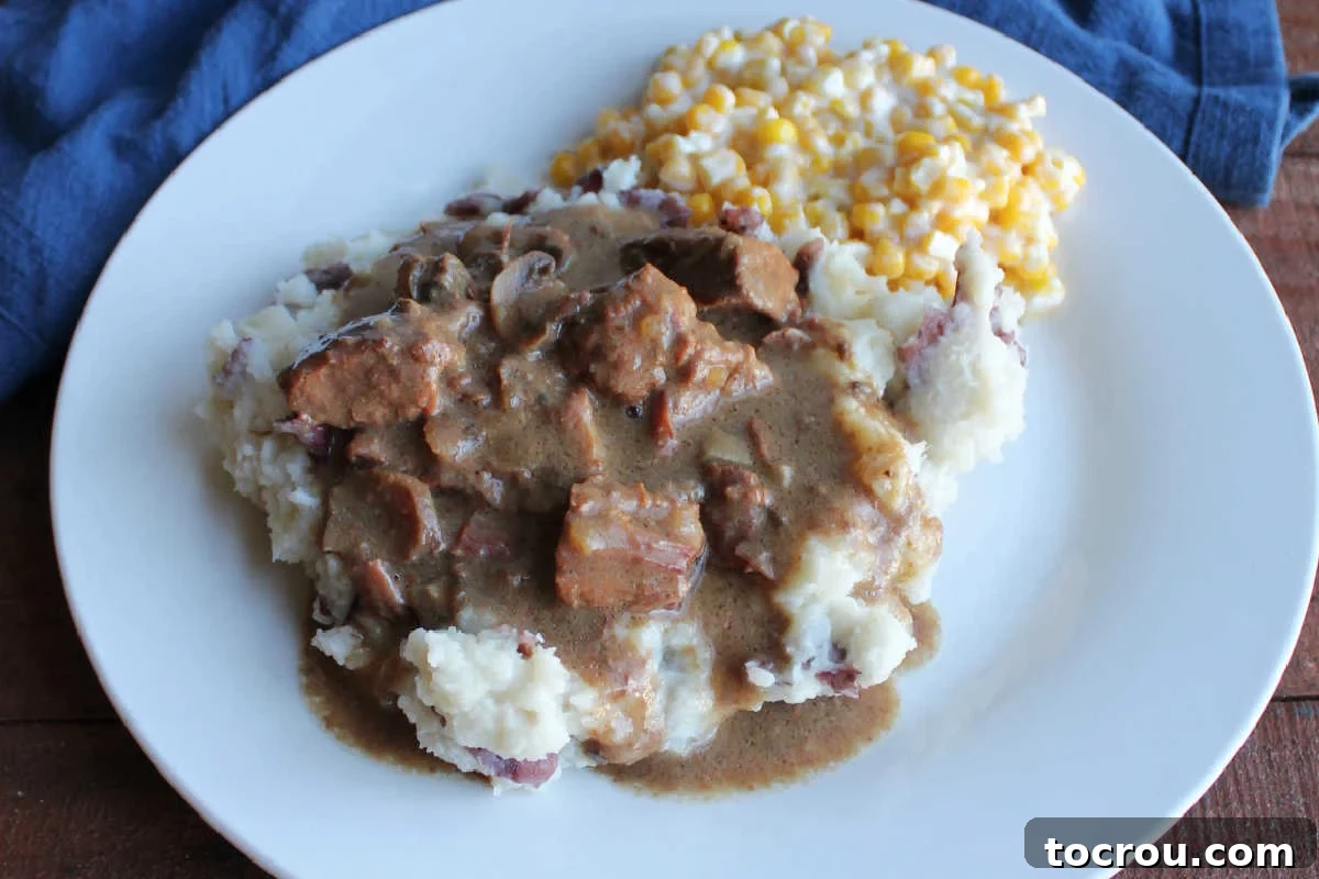 Plate of crockpot mystery roast beef bites and gravy on potatoes with corn, ready to eat.