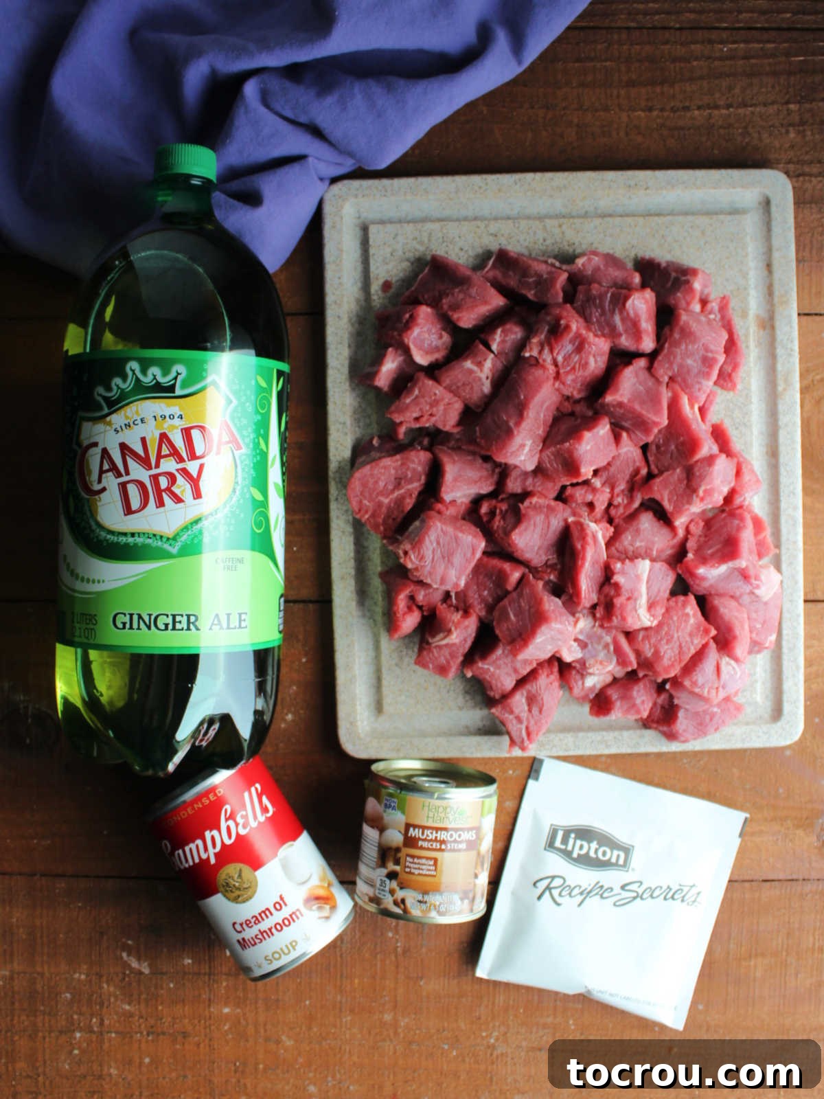 Ingredients including chunks of beef roast, ginger ale, cream of mushroom soup, packet of onion soup, and can of mushrooms ready to go in crockpot and make mystery roast.