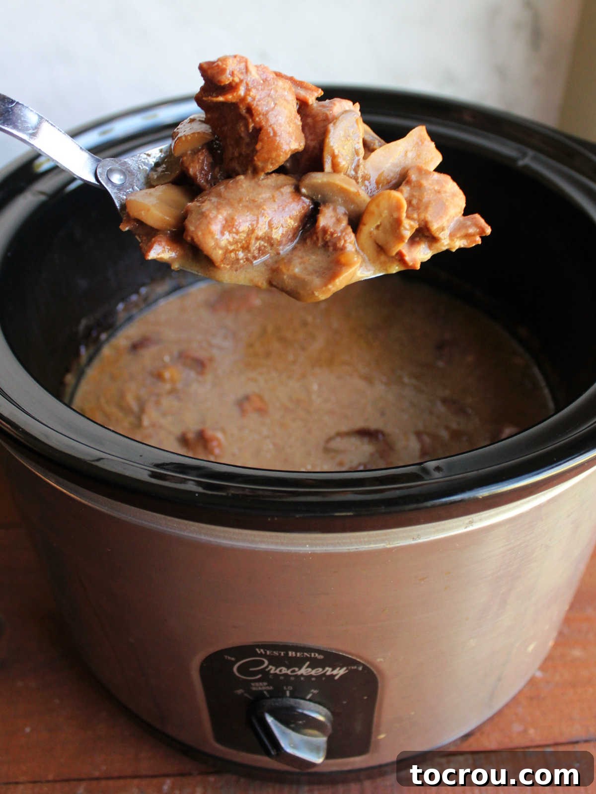 Spoonful of cooked mystery roast beef and mushrooms in creamy gravy after it has been cooked in crockpot.