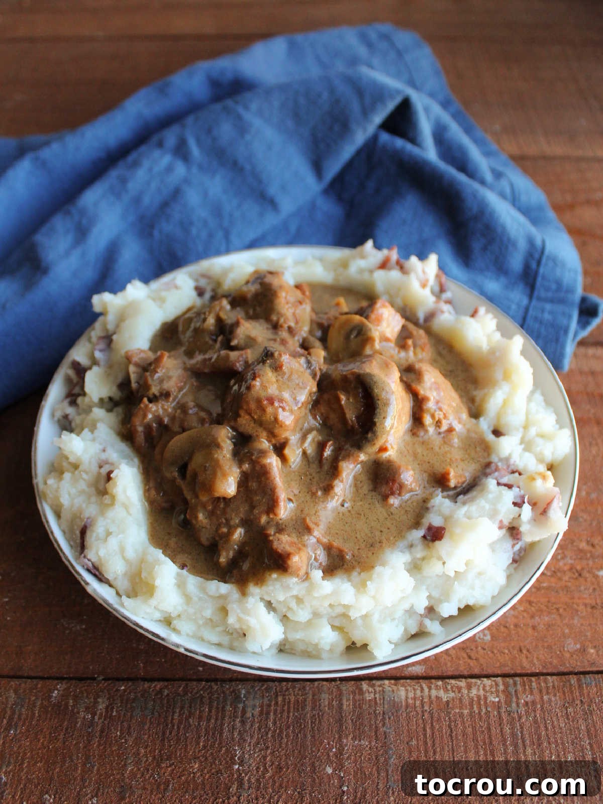 Bowl of smashed potatoes topped with bites of roast beef and gravy.