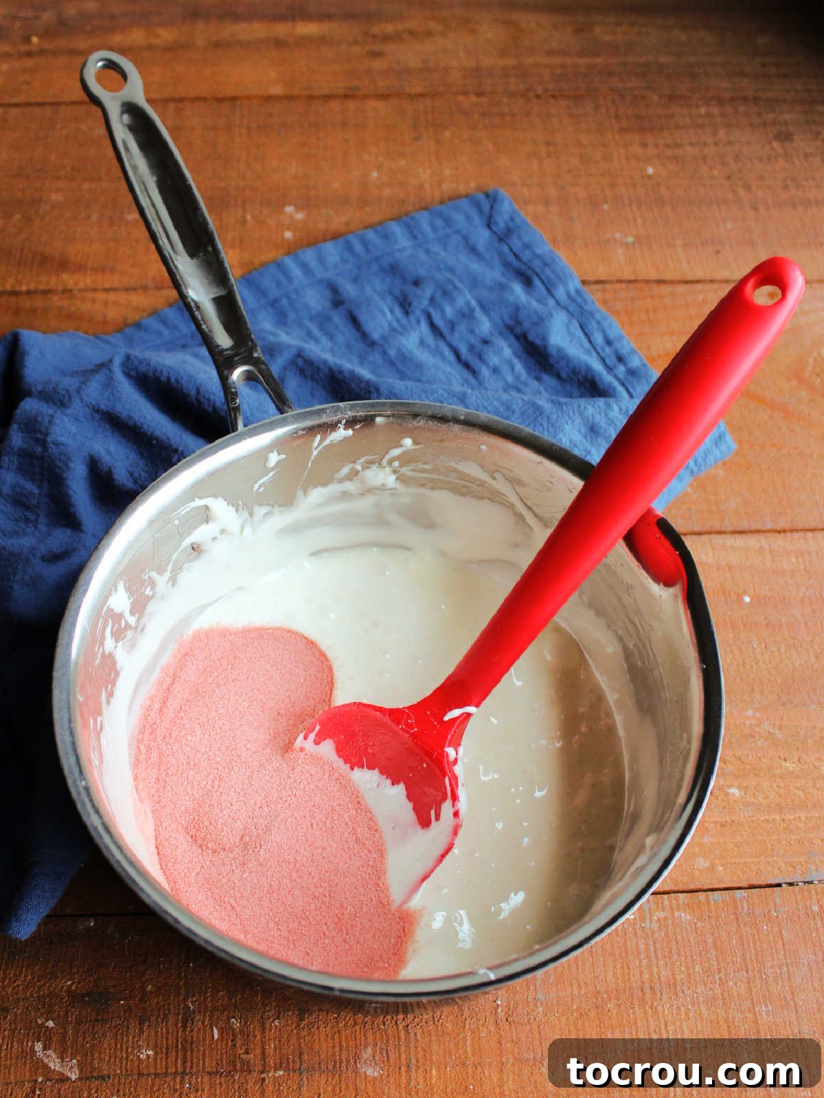 Saucepan with smooth melted butter and marshmallow mixture with red Jell-O powder ready to be stirred in for cherry popcorn balls.