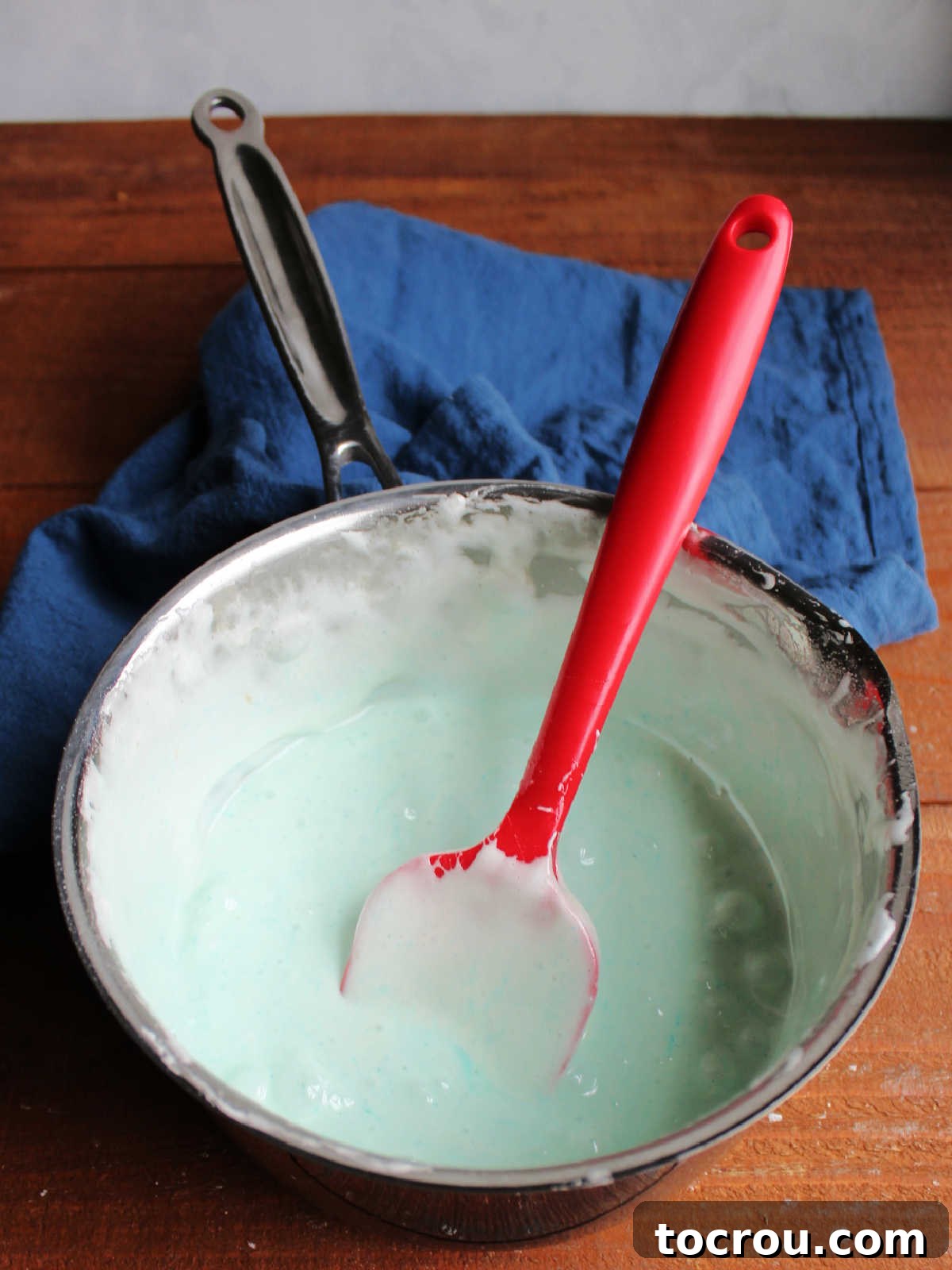 Saucepan filled with melted marshmallow and butter mixture, dyed blue with blue raspberry Jell-O powder, ready to be poured over popcorn.